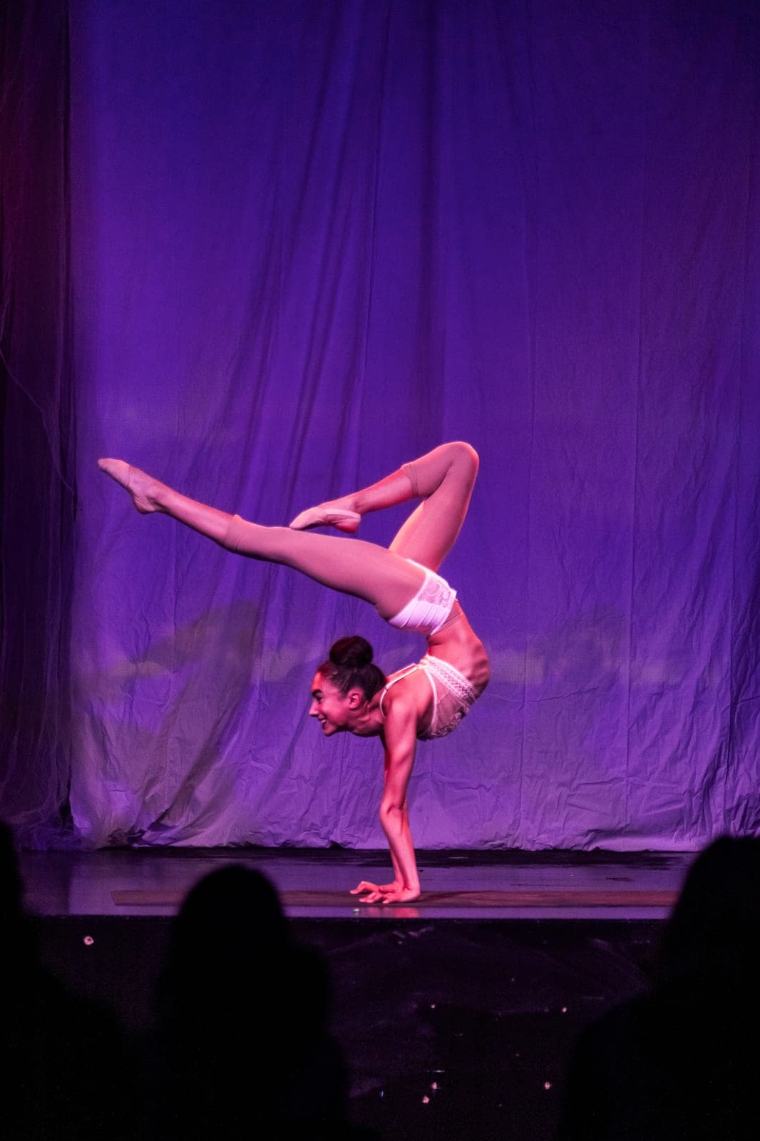 A contortionist holding an arched pose against a purple drape