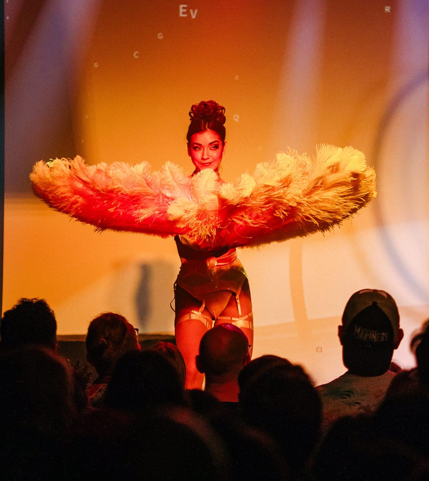 A burlesque performer mid-gesture behind a large feather fan